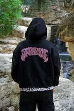 Person wearing a black hoodie with pink text in an outdoor setting