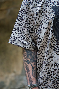 Person wearing a leopard print shirt with a tattooed arm against a blurred background