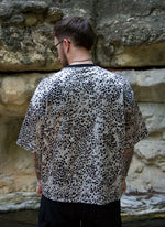Person wearing a leopard print shirt standing against a stone wall.
