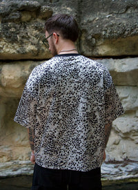 Person wearing a leopard print shirt standing against a stone wall.